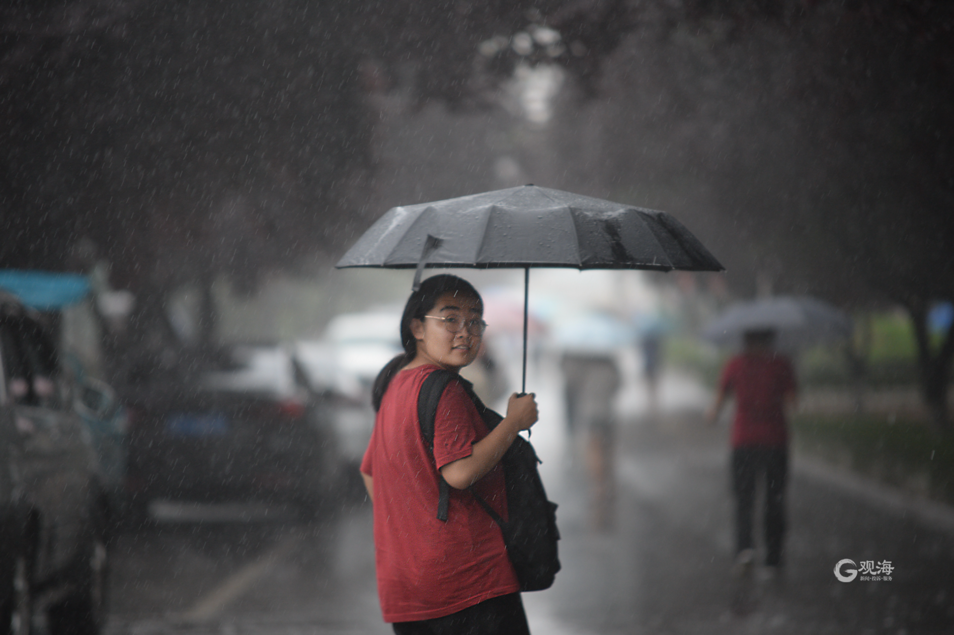 市区暴雨如注,强降雨导致道路积水,路上的车辆缓慢行驶,行人撑伞出行